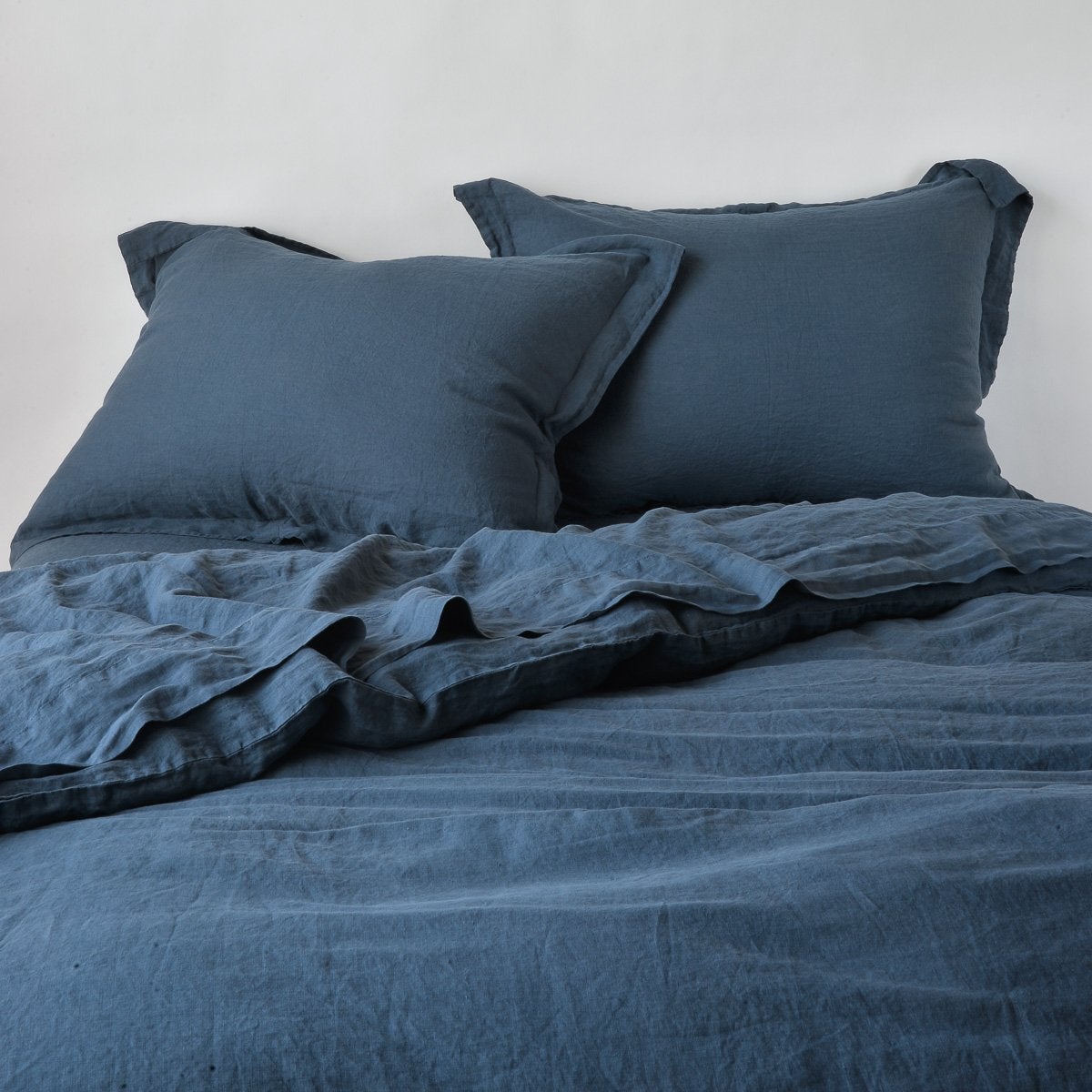 Midnight: duvet cover partially folded back on a bed with matching sheets and shams against a white wall - cropped end of bed view.