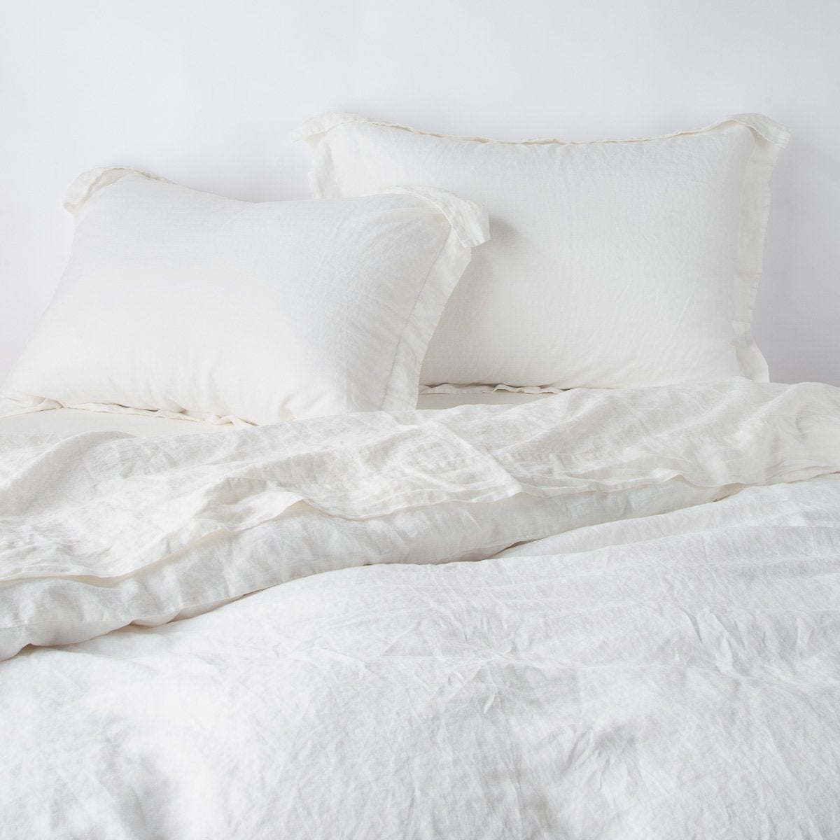 Winter White: duvet cover partially folded back on a bed with matching sheets and shams against a white wall - cropped end of bed view.