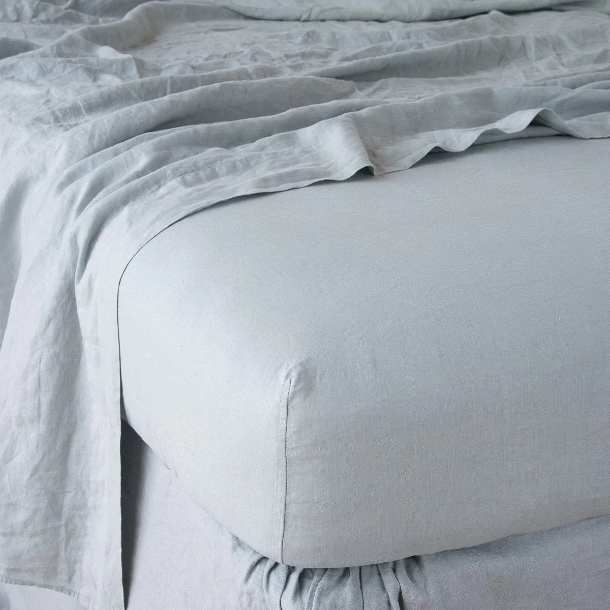 : Linen fitted sheet in mineral with matching rumpled flat sheet - shown from top corner.