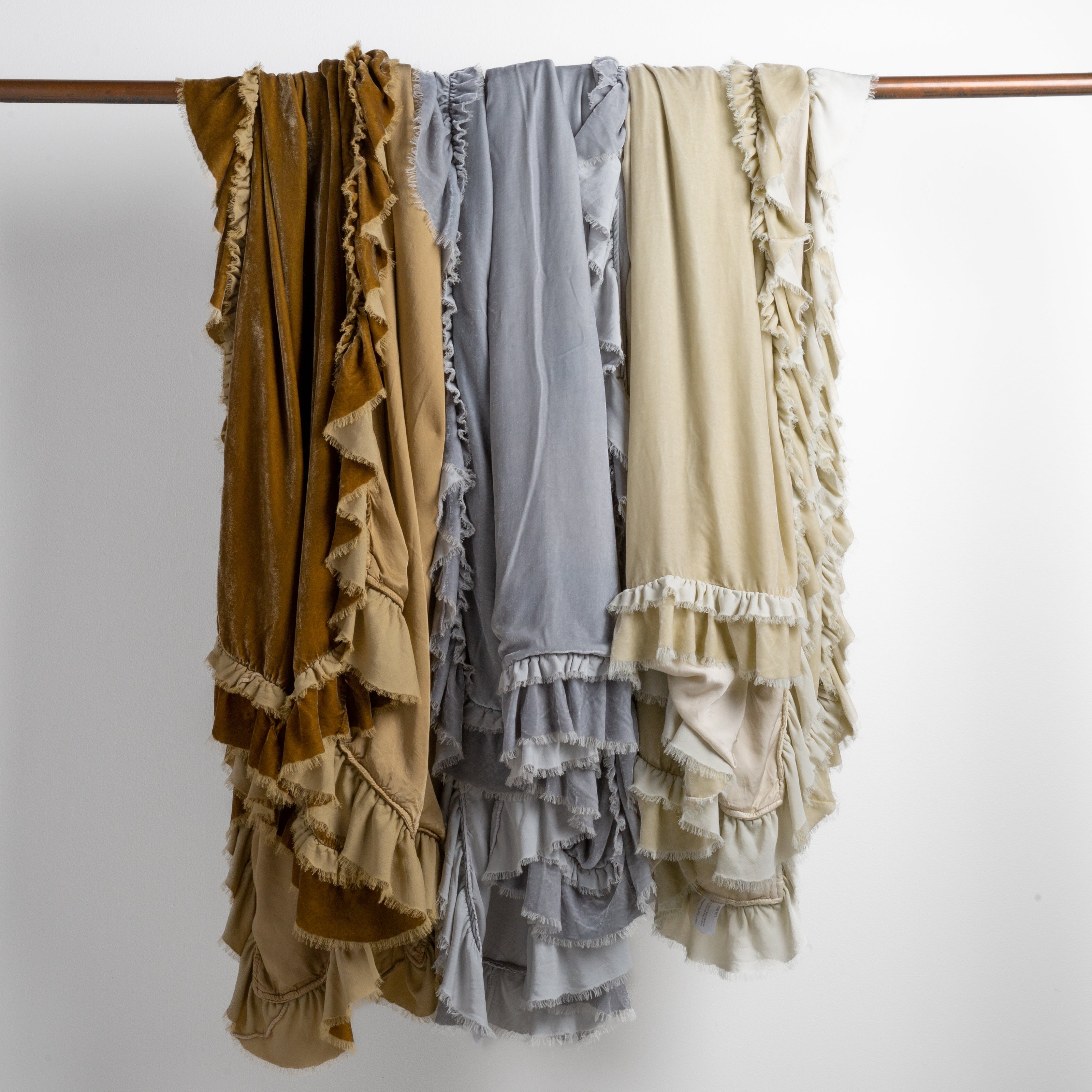 : three silk velvet blankets in honeycomb, sterling and parchment draped over a copper bar straight on against a white background.