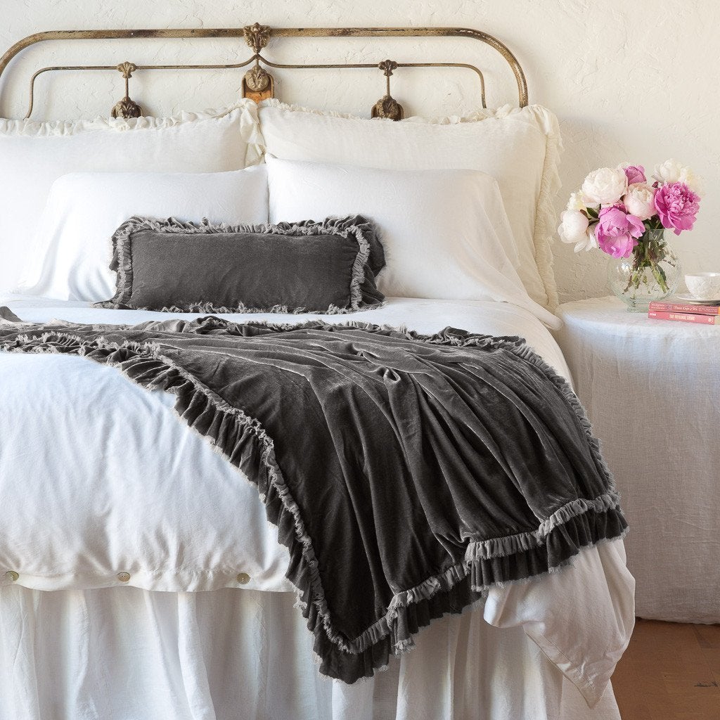 : Loulah throw blanket draped over the end of a white bed, shown with matching accent pillow - fog, end of bed view.
