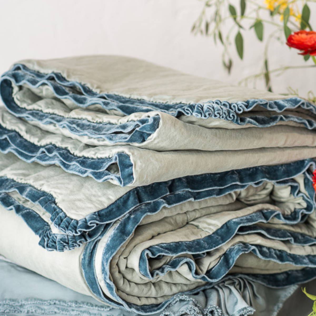 : Close-up of Paloma throw blanket in mineral, neatly folded, highlighting the richly dyed silk velvet trim.
