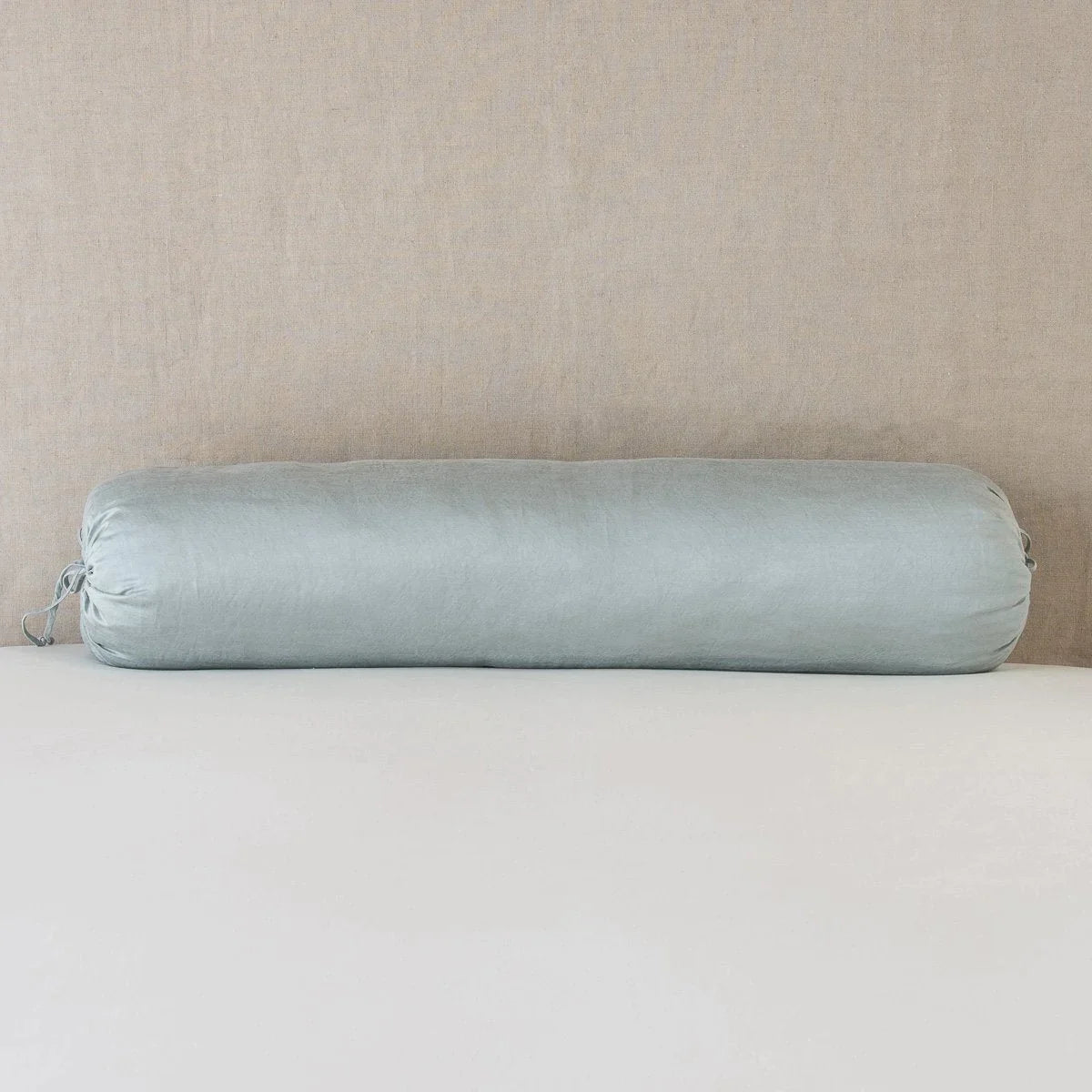 : Paloma bolster against white sheets against a neutral headboard - mineral.