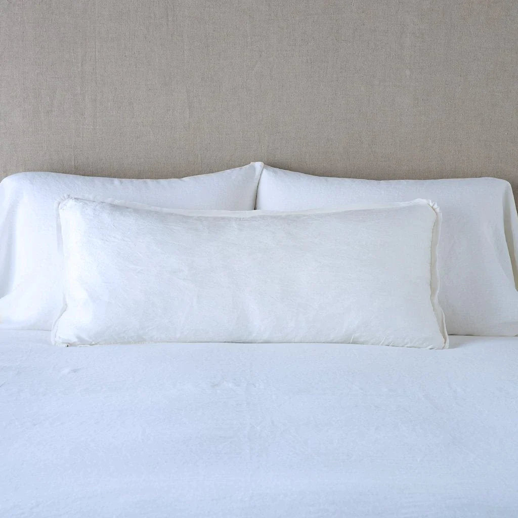 White: 16x36 charmeuse pllow wth silk velvet trim against white sleeping pillows and sheets — straight on with neutral background.