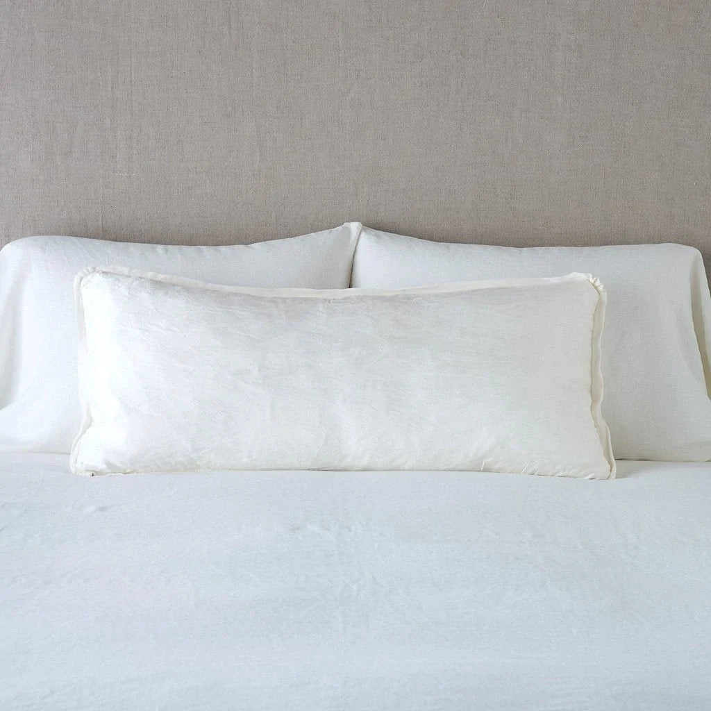 Winter White: 16x36 charmeuse pllow wth silk velvet trim against white sleeping pillows and sheets — straight on with neutral background.