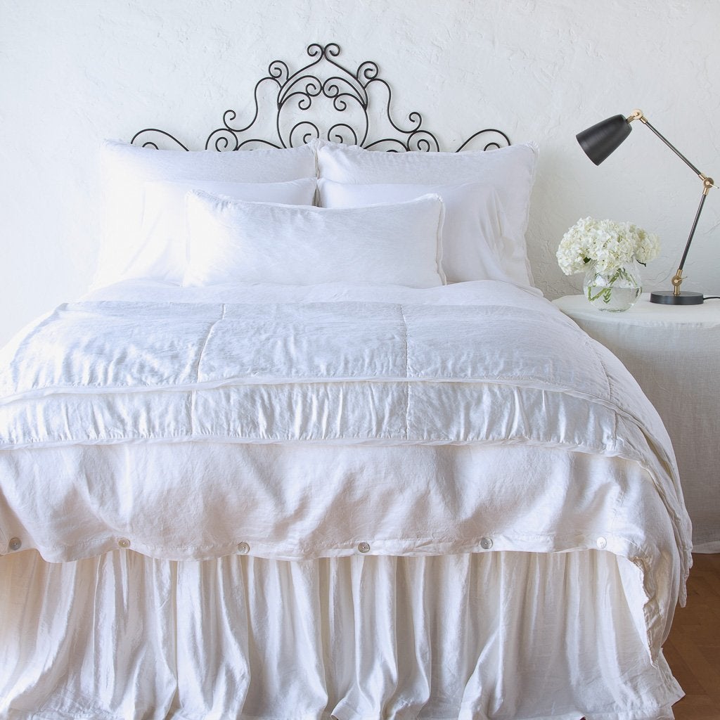 White: throw blanket folded at the end of a monochromatic, charmeuse bed - end of bed view.