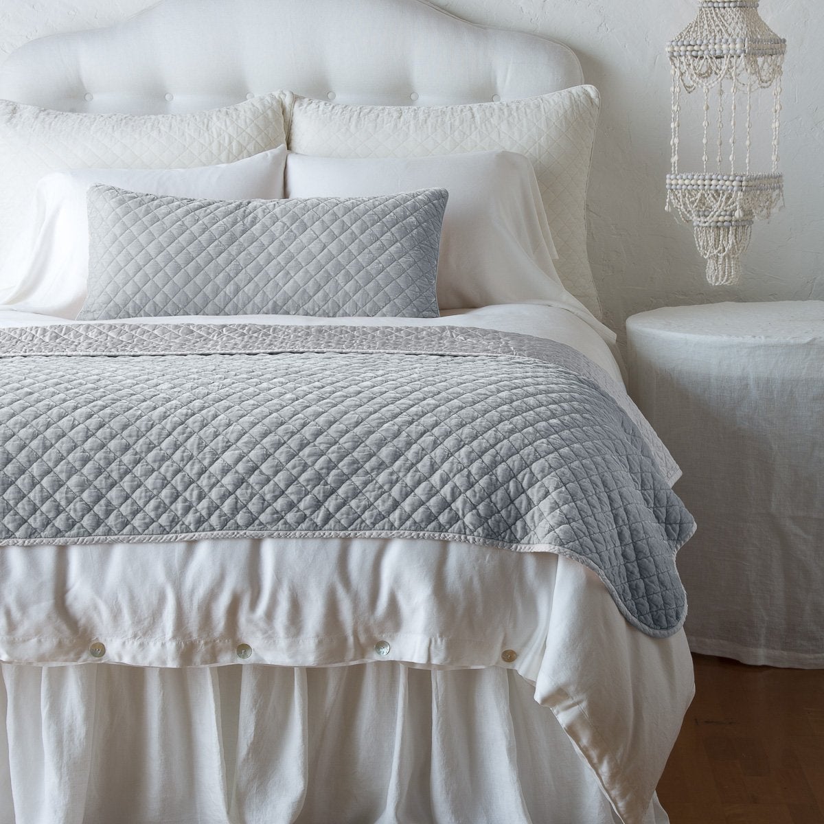 : Silk velvet throw blanket and matching lumbar pillow on a neatly made white bed - cloud, end of bed view.
