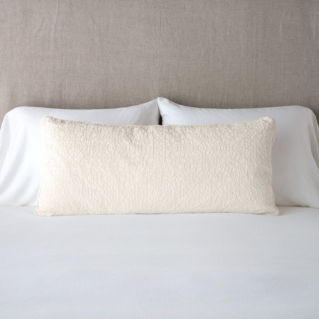 Parchment: 16x36 pillow leaning upright against white sleeping pillows on a neutral headboard.