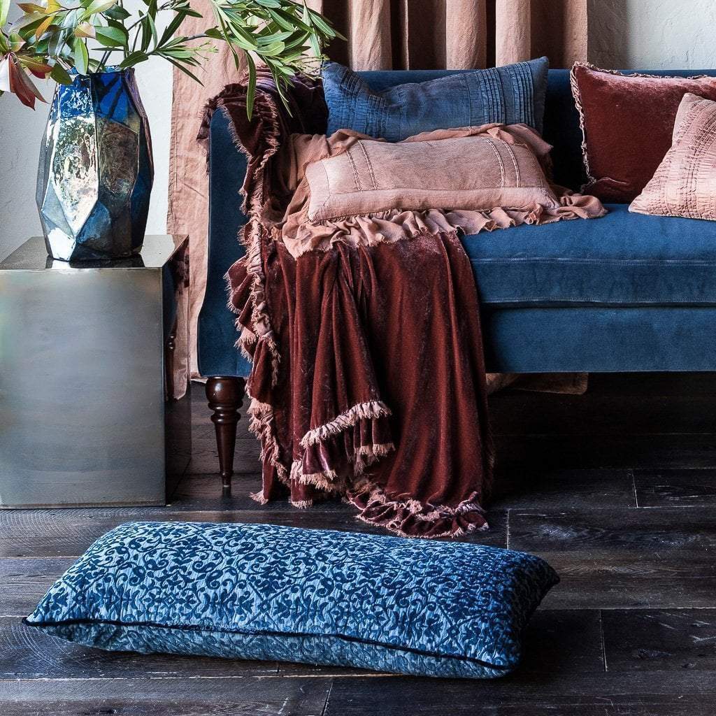 : Midnight blue Vienna 16x36 pillow on a wood floor, with matching velvet sofa in the background layered with soft pink and brown tones.