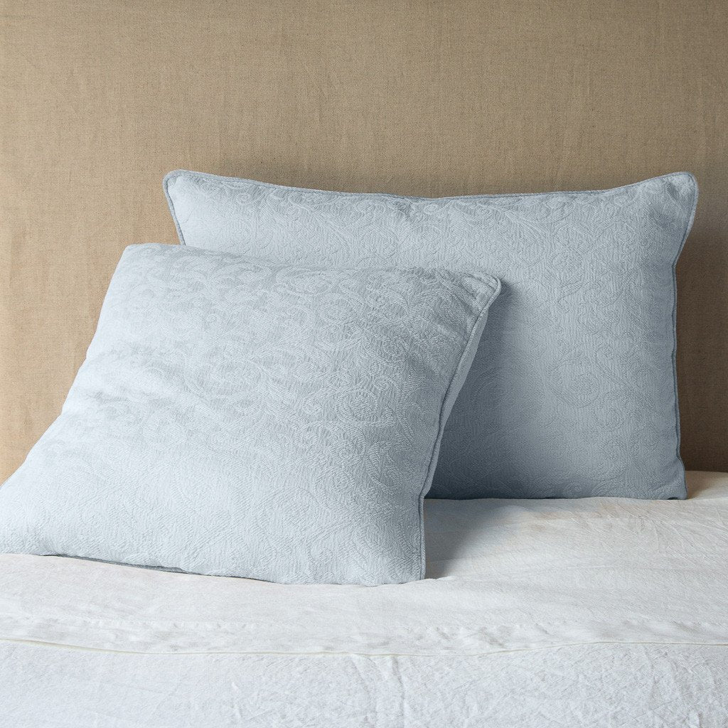 [allvariants]: Adele shams in eucalyptus on a bed shown from the side, layered with white sheets and pillowcases and a eucalyptus coverlet against a plain white wall.