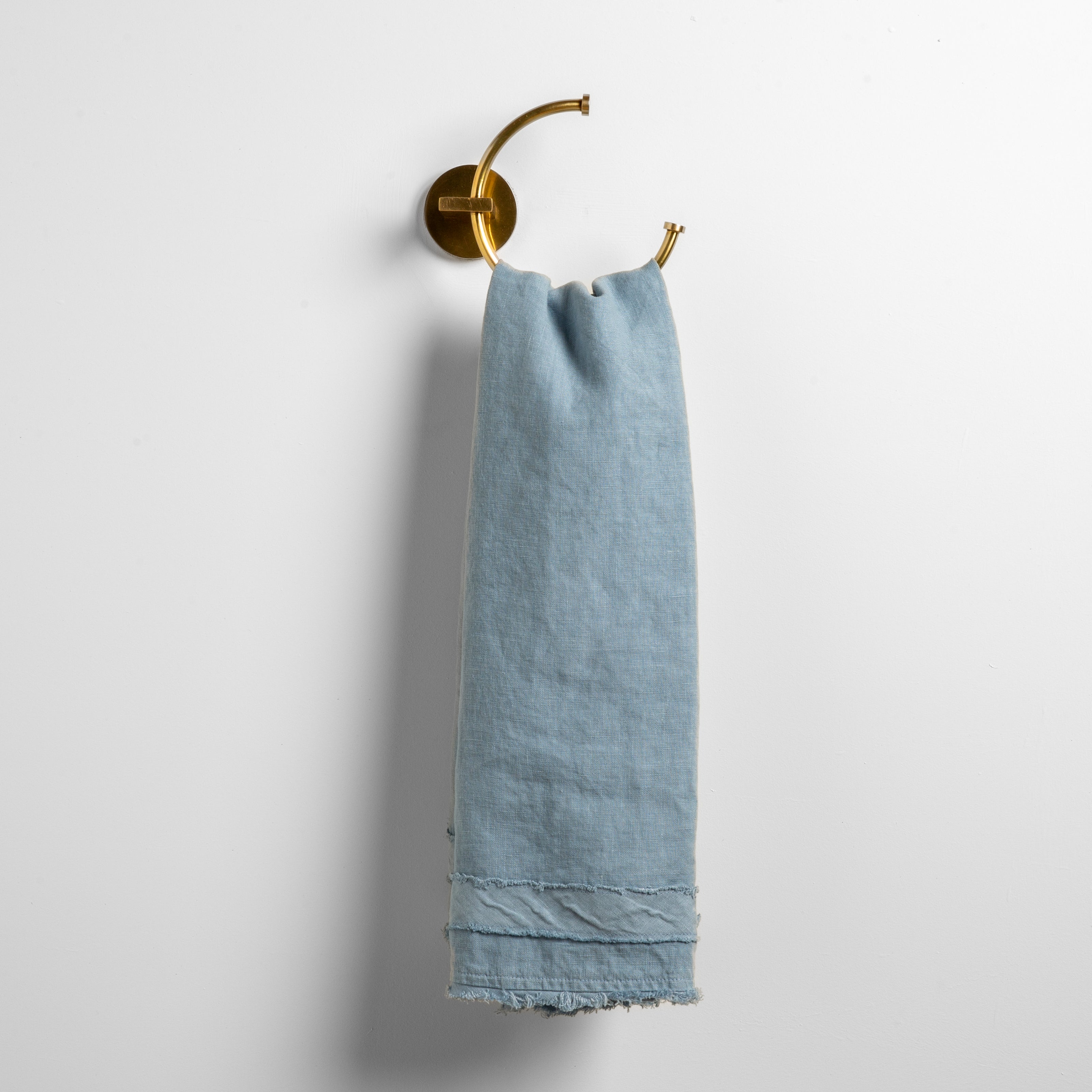 Tahoe Blue: midweight linen guest towel with raw edge band at both ends hanging from a towel ring mounted to a white wall. 
