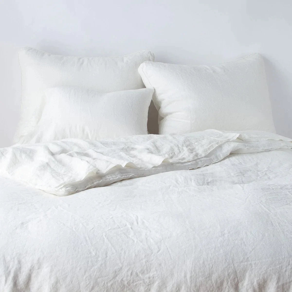 Winter White: Midweight linen shams shown from foot of bed, leaning against a plain background with monochromatic bedding. 