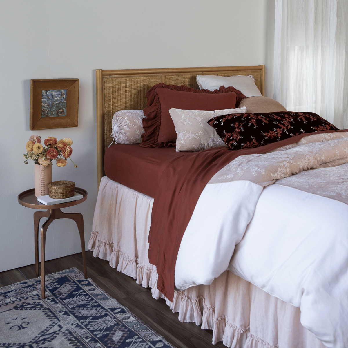 [allvariants]: a pale pink duvet cover with dark terrcotta colored sheets and pillows against a rattan headboard with coordinating side table - shot from a 3/4 angle. 