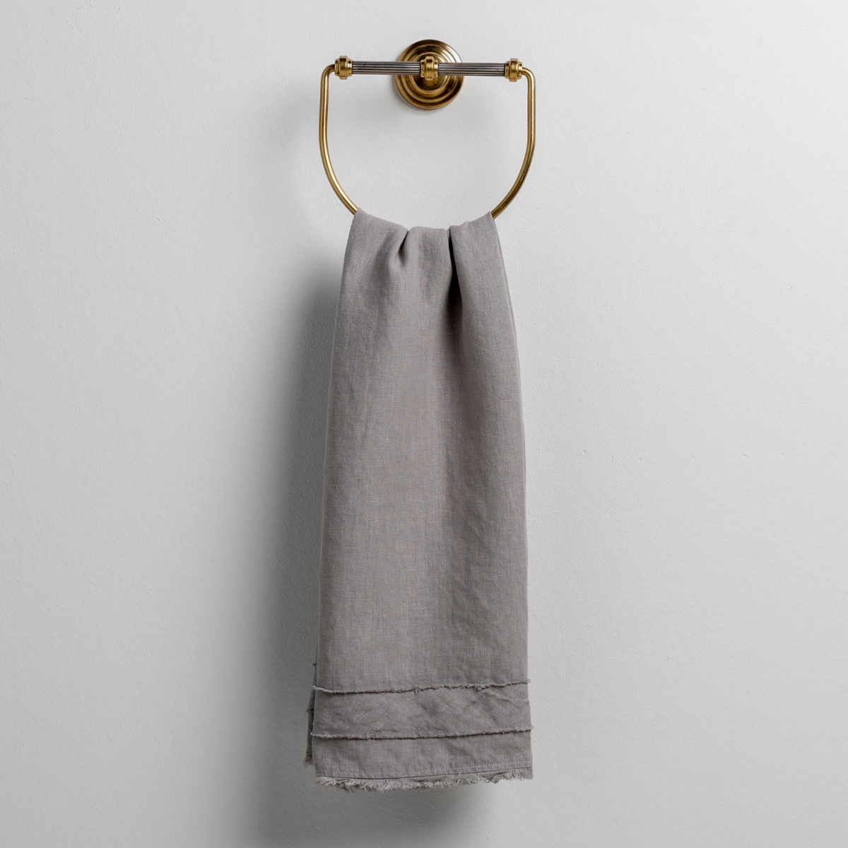 Fog: midweight linen guest towel with raw edge band at both ends hanging from a towel ring mounted to a white wall. 