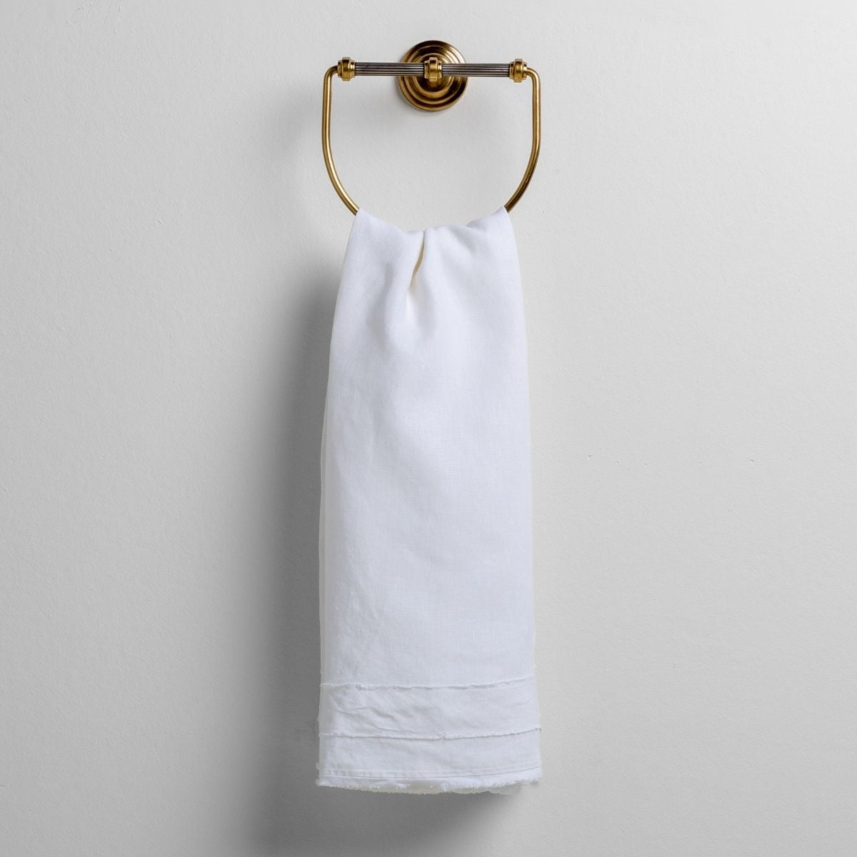 White: midweight linen guest towel with raw edge band at  both ends hanging from a towel ring mounted to a white wall. 
