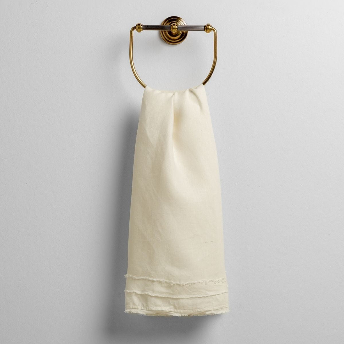 Winter White: midweight linen guest towel with raw edge band at  both ends hanging from a towel ring mounted to a white wall. 