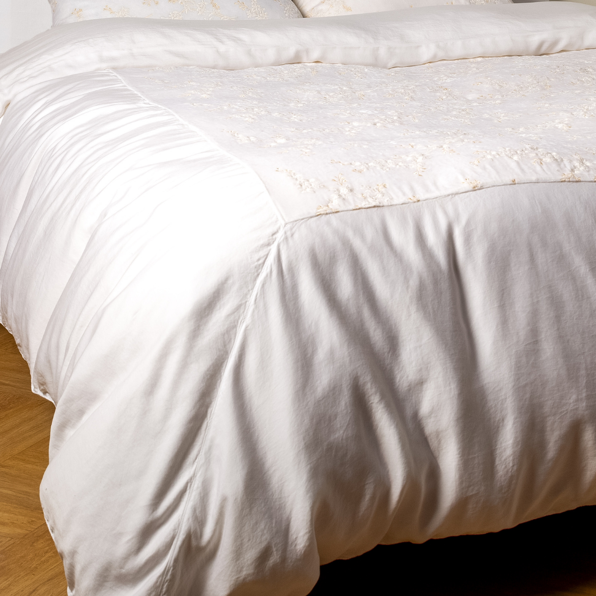 White: A close-up of the mitered corner of an embroidered silk velvet and tencel duvet cover — its matching shams barely visible in the shot. 
