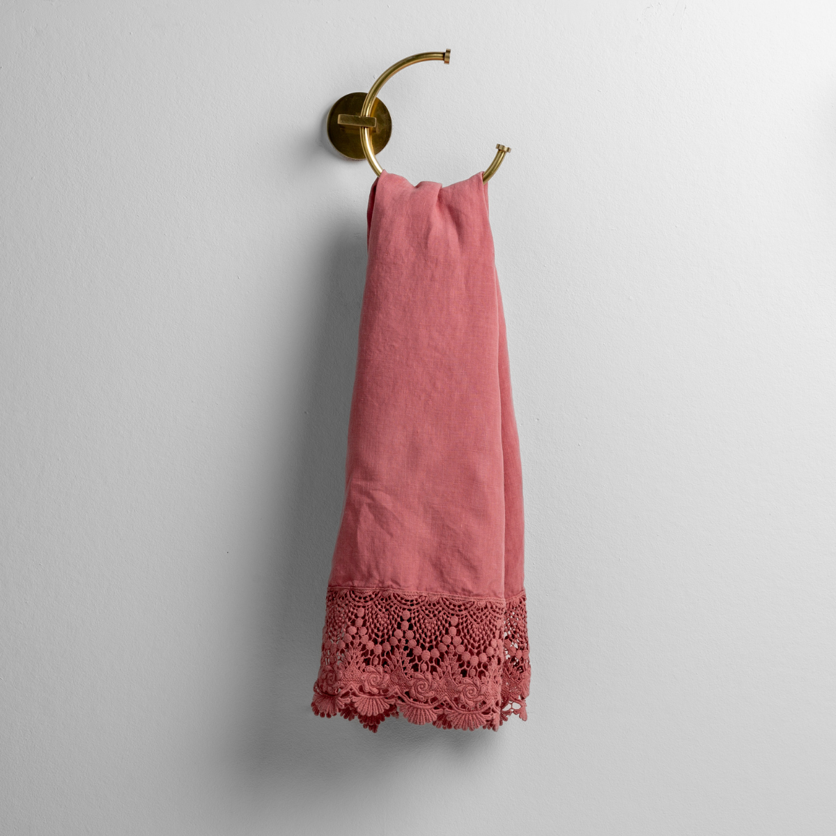 Poppy: linen with mattine lace trimmed guest towel on a decorative towel ring mounted on a white wall. 