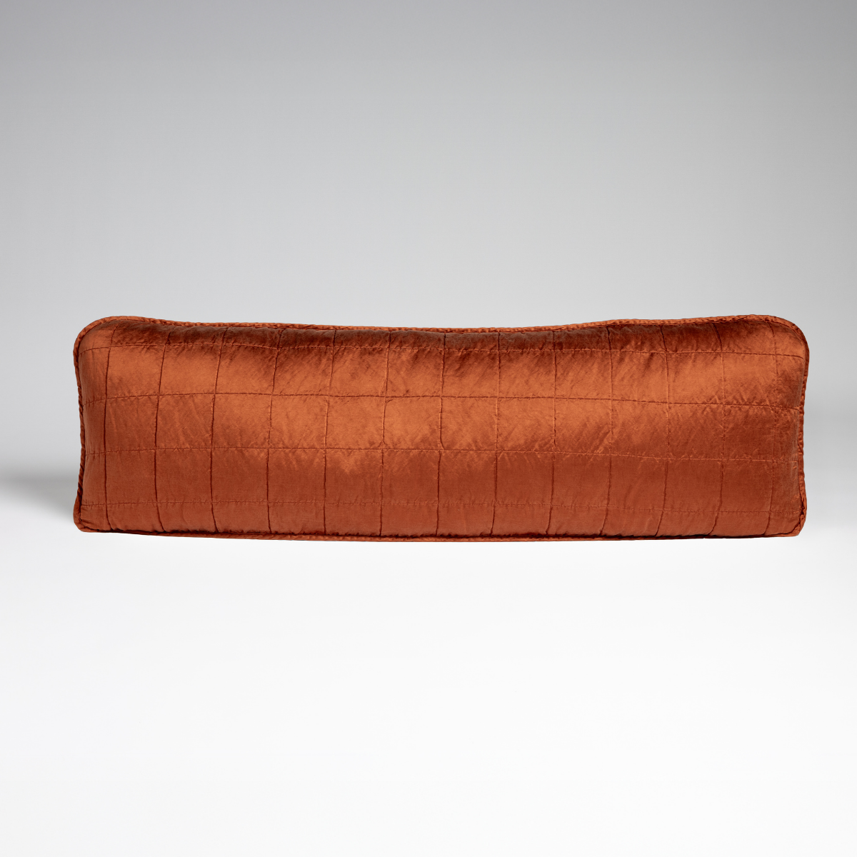 Autumn: A straight-on shot of a square-quilted body pillow in autumn, a rich terracotta tone, against a white background. 