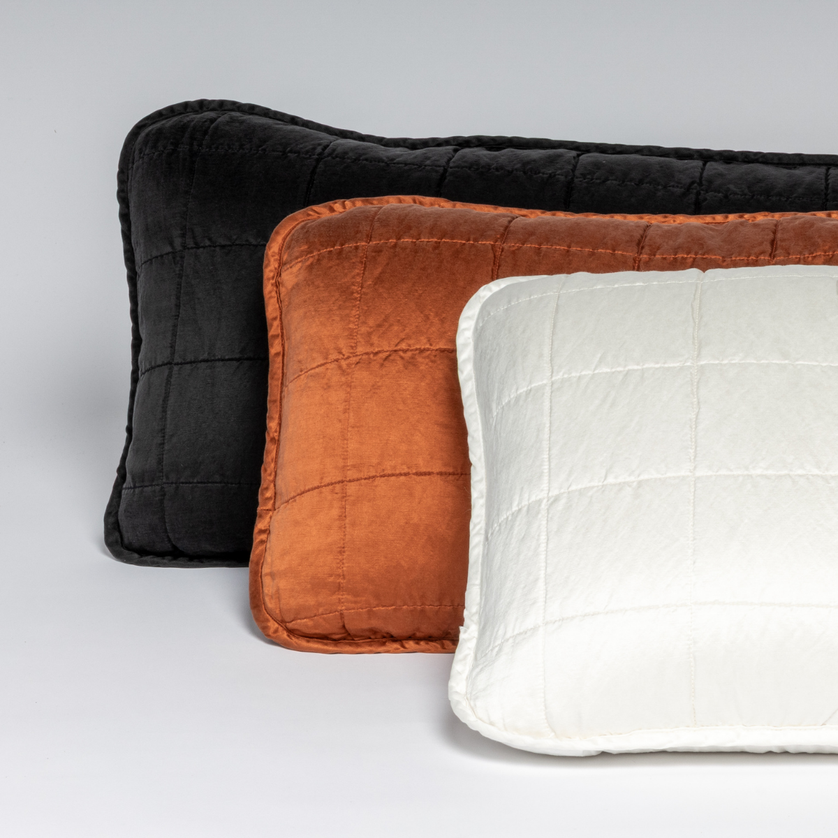 Three rectangular quilted throw pillows stacked against each other on a white background, shot straight on.
