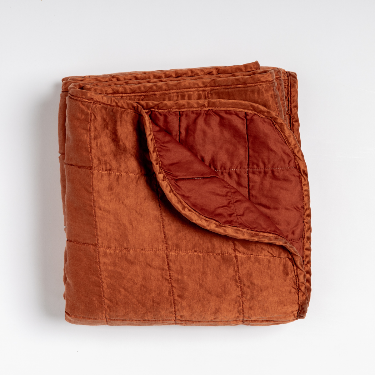 Autumn: an overhead shot of a quilted charmeuse blanket with a corner folded down, showing its cotton sateen back. 