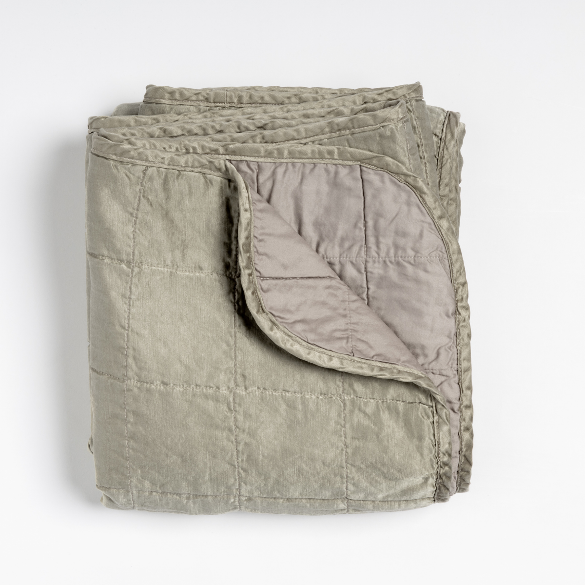 Fog: an overhead shot of a quilted charmeuse blanket in fog, a soft mid-tone grey, with a corner folded down, showing its cotton sateen back. 