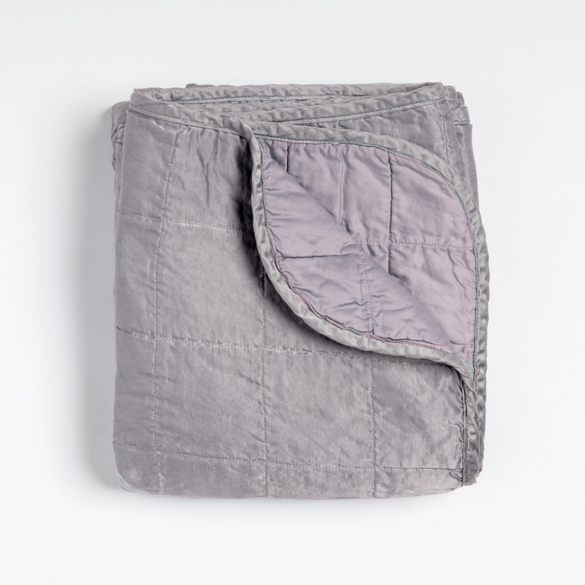 French Lavender: an overhead shot of a quilted charmeuse blanket in french lavender, a neutral violet tone, with a corner folded down, showing its cotton sateen back. 