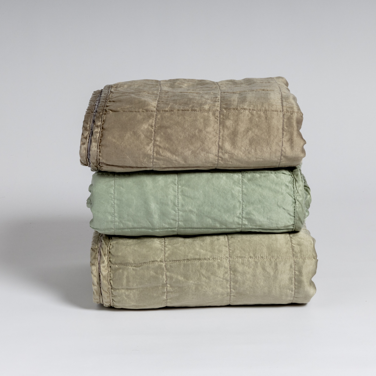 A stack of three square-quilted charmeuse blankets shot straight on against a white background. 