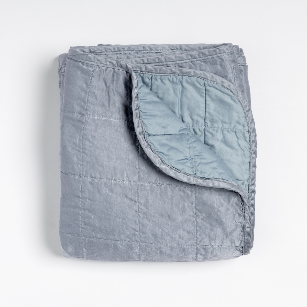 Tahoe Blue: an overhead shot of a quilted charmeuse blanket in tahoe blue, a crisp true blue, with a corner folded down, showing its cotton sateen back. 
