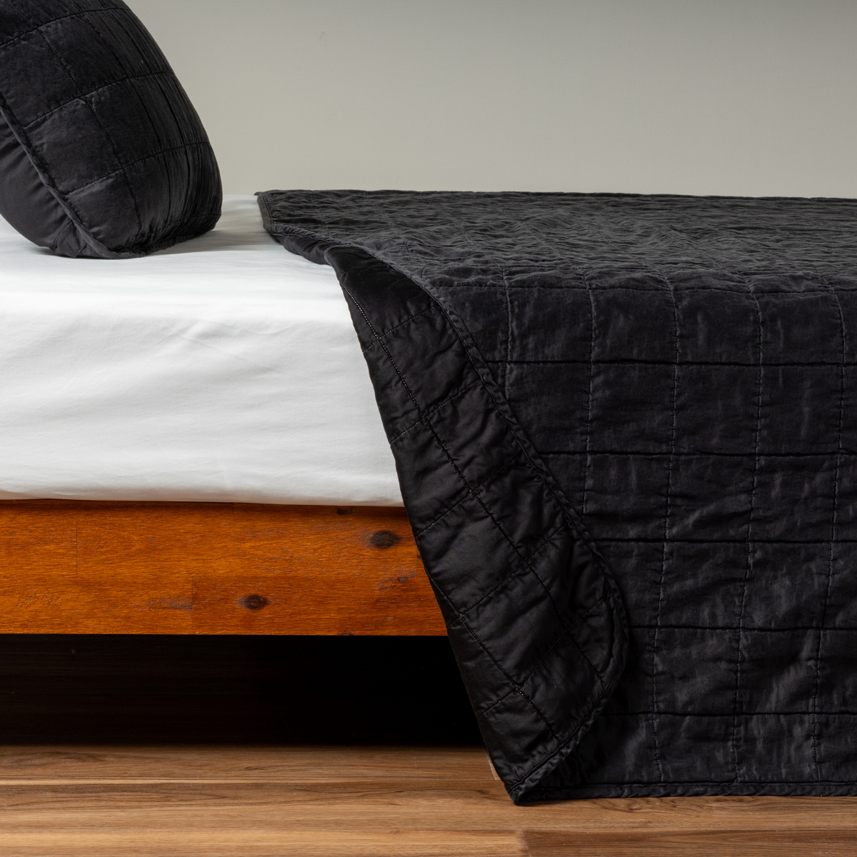 Corvino: A side shot of a square quilted charmeuse coverlet with its matching sham in corvino, our classic black, the corner of the coverlet peeled back, revealing the cotton sateen back. 
