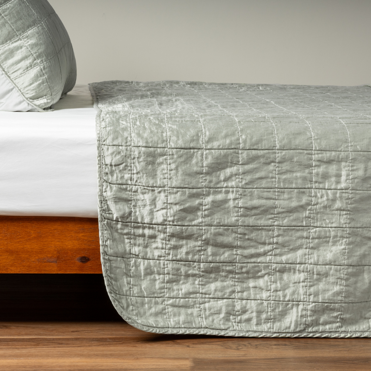 Eucalyptus: A side shot of a square quilted charmeuse coverlet in eucalyptus, a soft light green, with its matching sham, the corner of the coverlet peeled back, revealing the cotton sateen back. 
