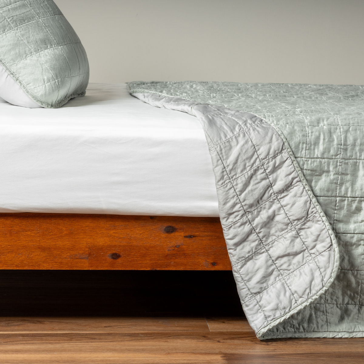 Mineral: A side shot of a square quilted charmeuse coverlet in mineral, a soothing seafoam blue with subtle grey-green undertones, with its matching sham, the corner of the coverlet peeled back, revealing the cotton sateen back. 