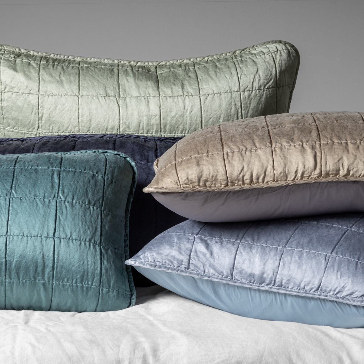 A cluster shot of five square-quilted charmeuse shams showing their unquilted cotton sateen back. 