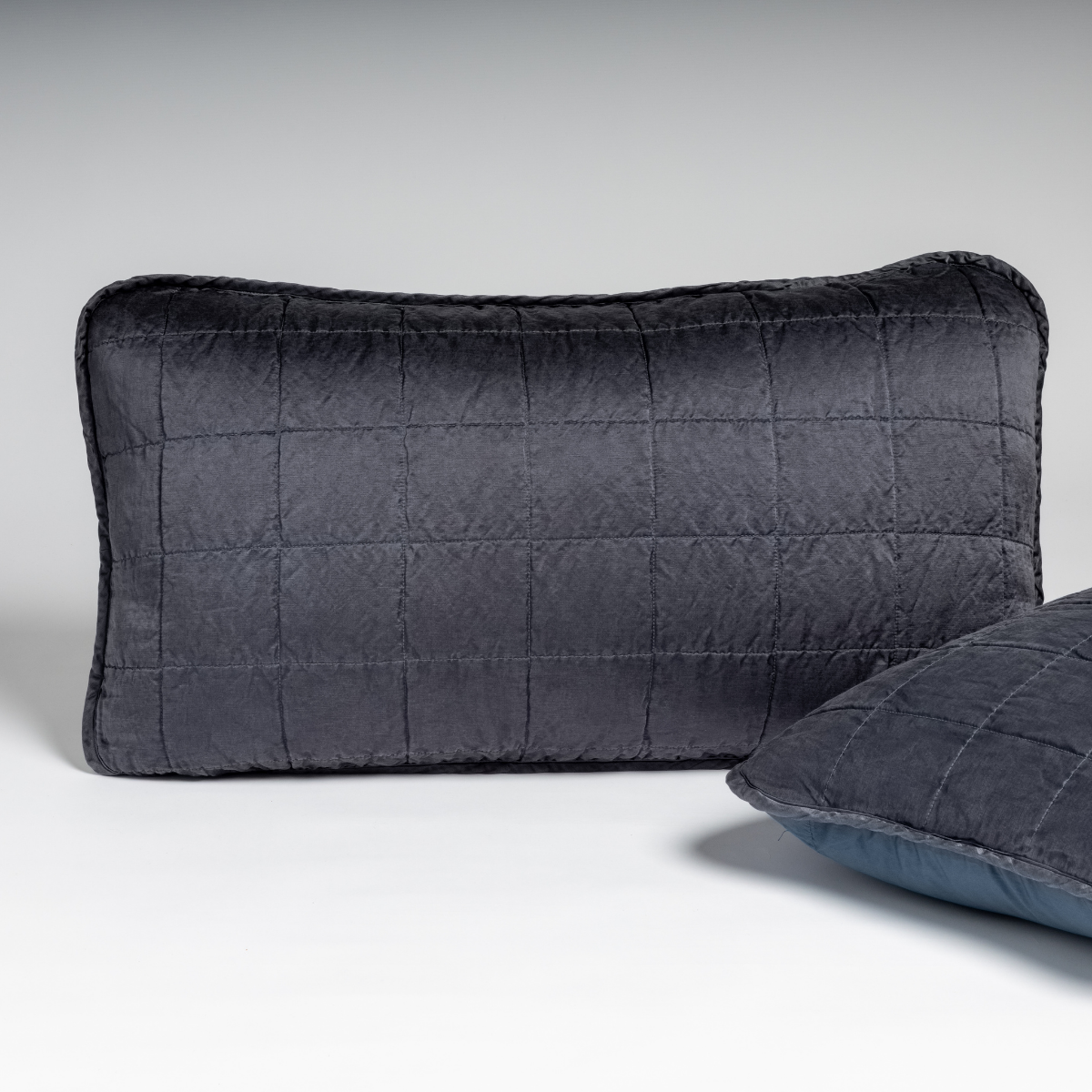 Midnight: A pair of shams in midnight, a rich indigo tone, shown against a white background with one sham upright and the other on its side to show the cotton sateen back and square-quilted charmeuse front. 