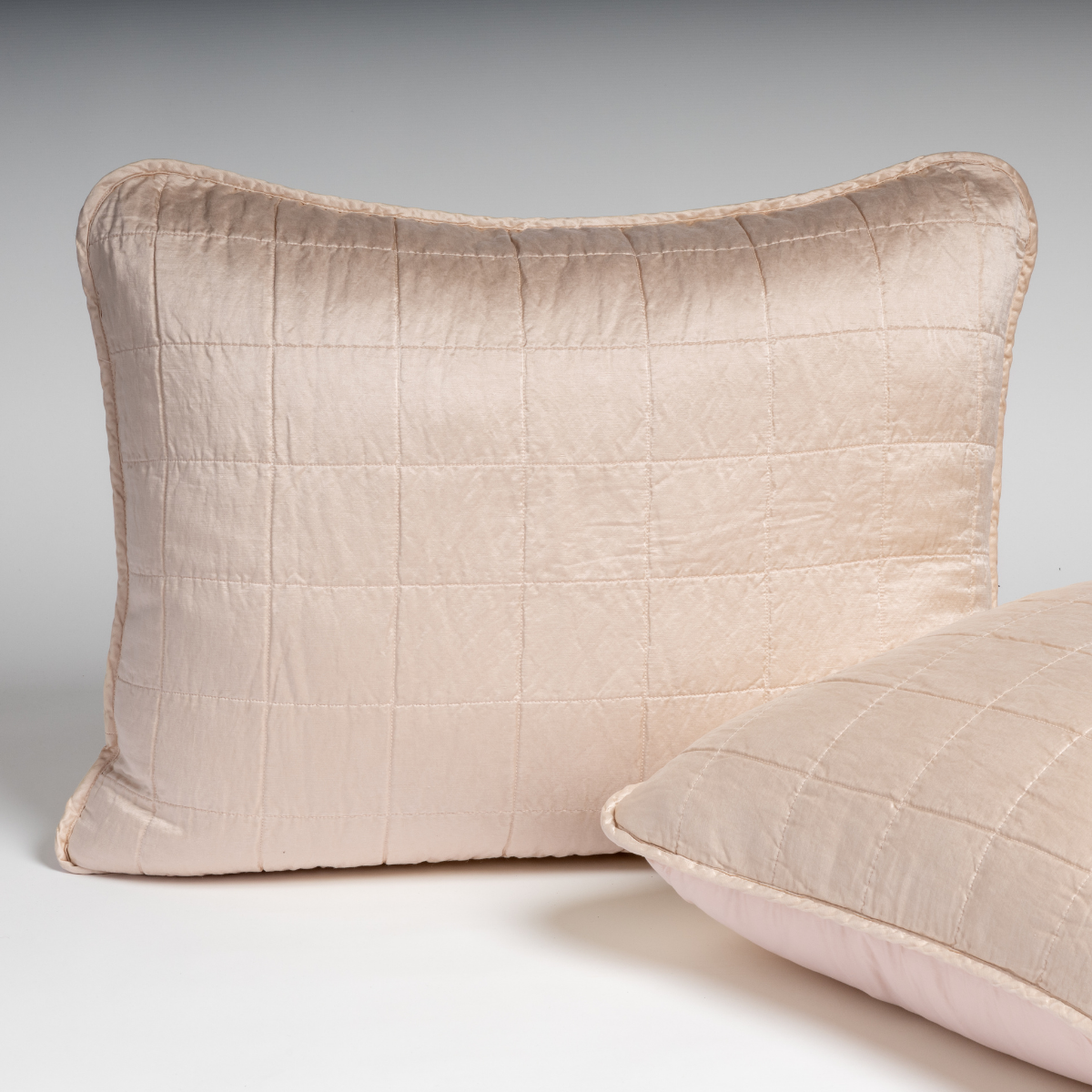Pearl: A pair of shams in pearl, a soft rose pink tone, shown against a white background with one sham upright and the other on its side to show the cotton sateen back and square-quilted charmeuse front. 
