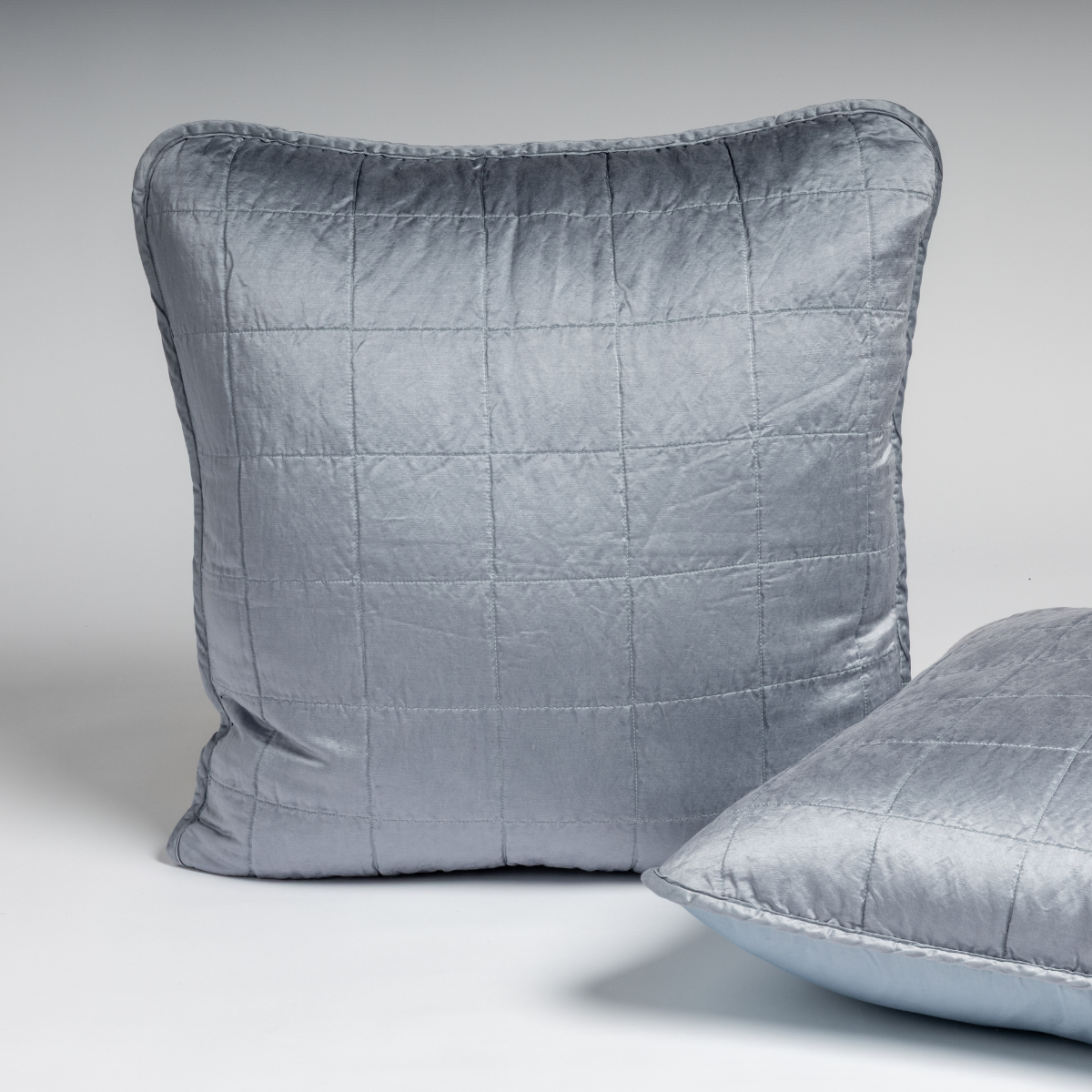 Tahoe Blue: A pair of Euro shams shown in tahoe blue, a crisp true blue, against a white background with one sham upright and the other on its side to show the cotton sateen back and square-quilted charmeuse front. 