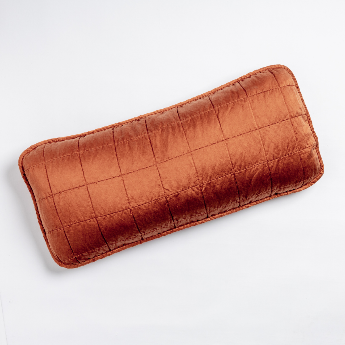 Autumn: An overhead shot of a square-quilted rectangle throw pillow in autumn, a rich terracotta tone, against a white background. 