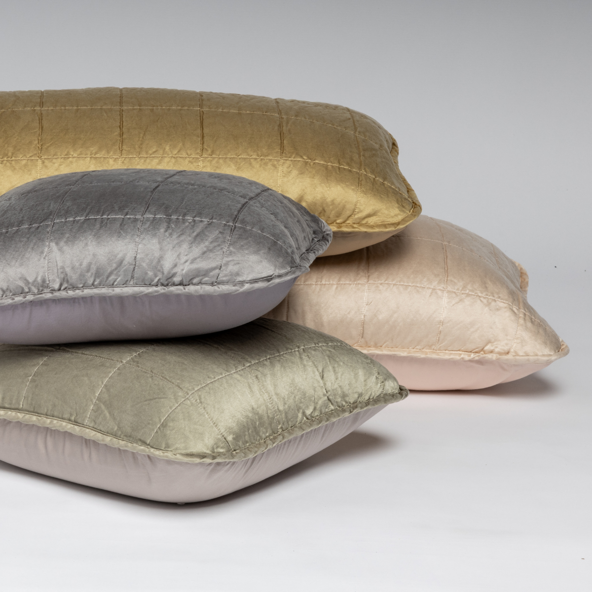 A cluster shot of assorted square-quilted throw pillows shown straight on against a white background. 
