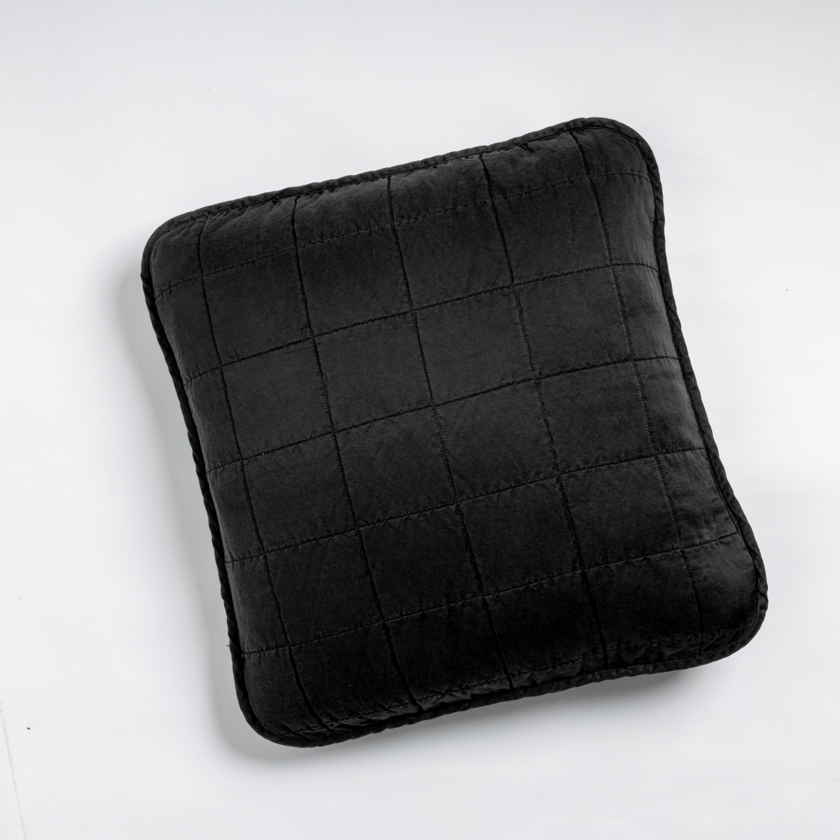 Corvino: An overhead shot of a square-quilted square throw pillow in corvino, our classic black, against a white background. 