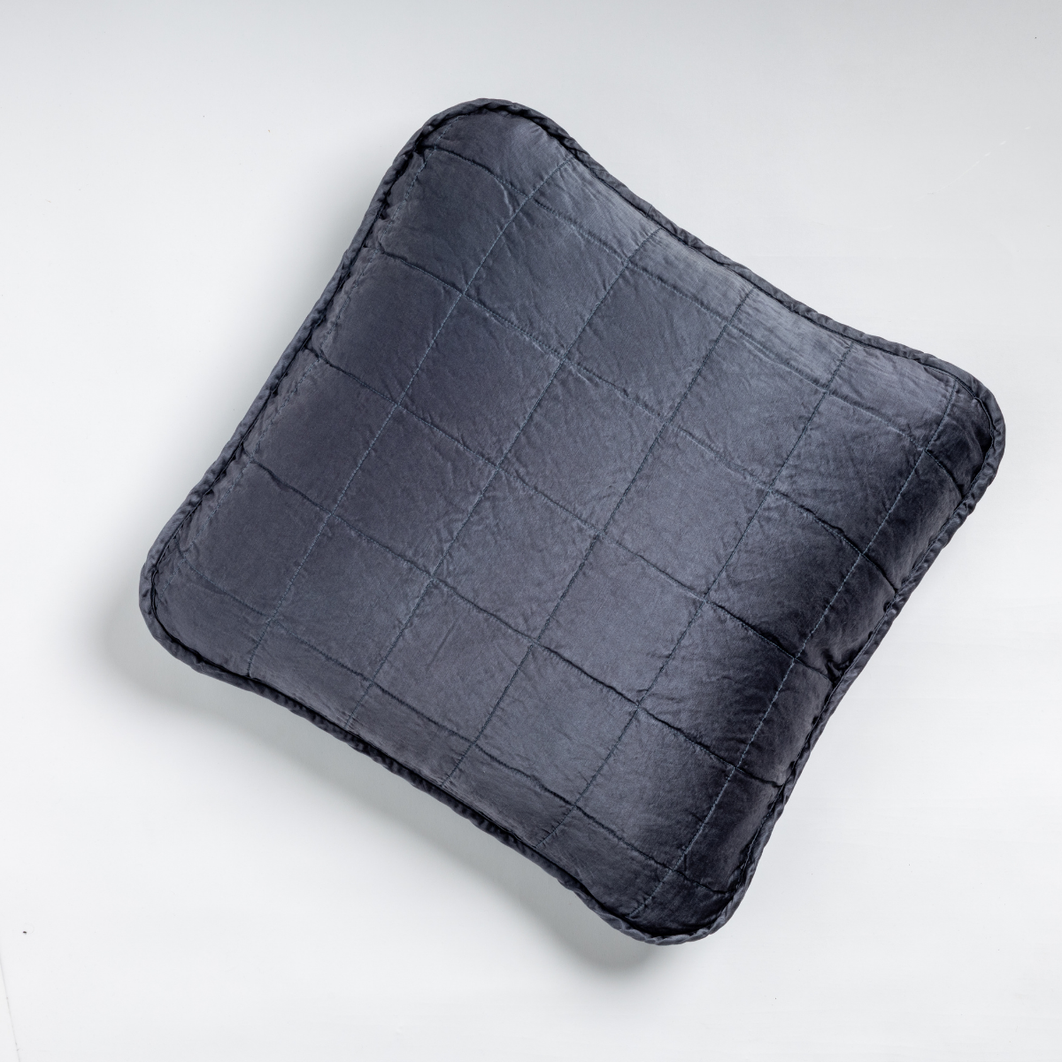Midnight: An overhead shot of a square-quilted square throw pillow in midnight, a rich indigo tone, against a white background. 