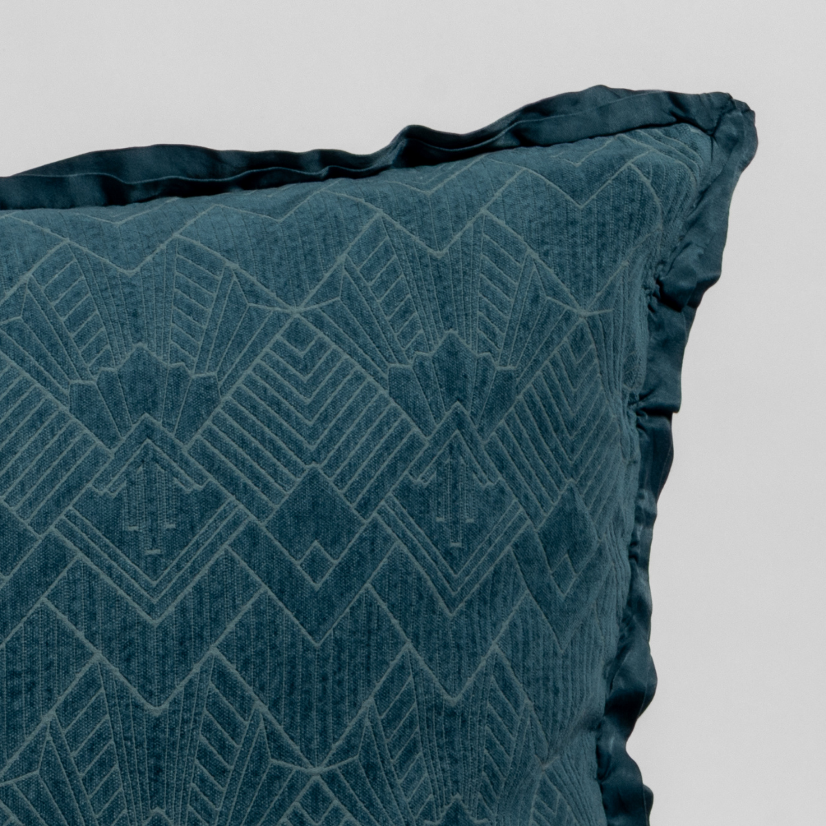 Cenote: Close-up of a textured pillow sham corner with a satin ruffle, shot against a plain background.