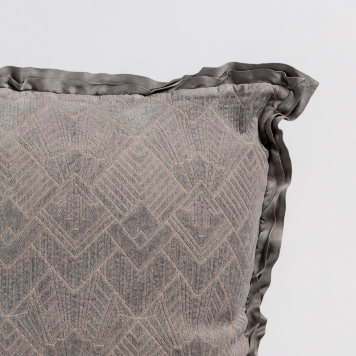 Fog: Close-up of a textured pillow sham corner with a satin ruffle, shot against a plain background.