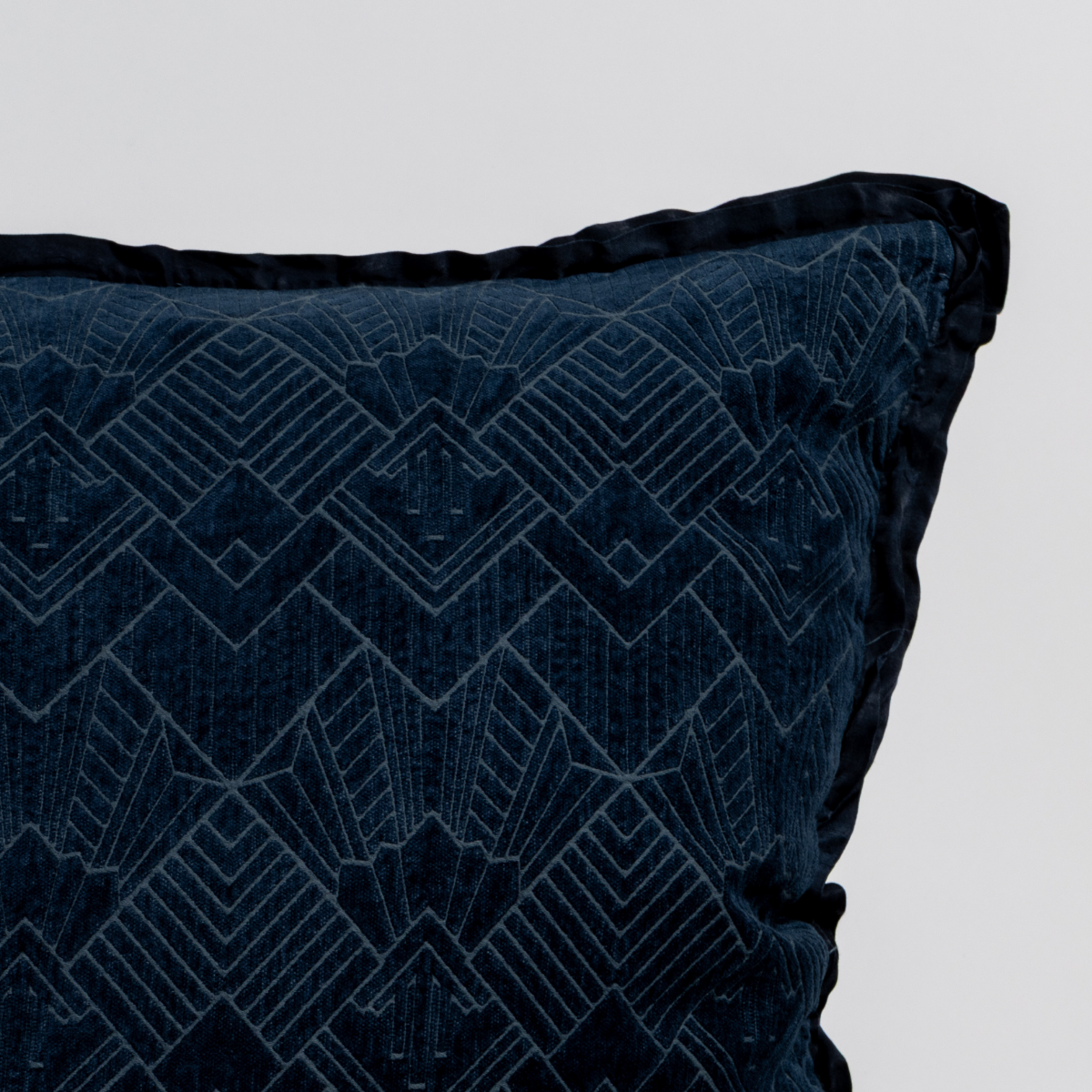Midnight: Close-up of a textured pillow sham corner with a satin ruffle, shot against a plain background.