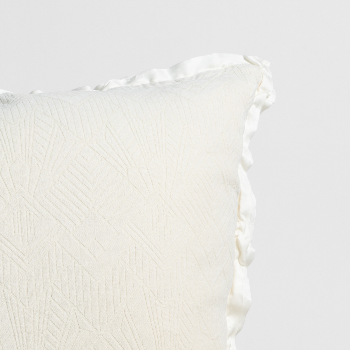 Natural: Close-up of a textured pillow sham corner with a satin ruffle, shot against a plain background.