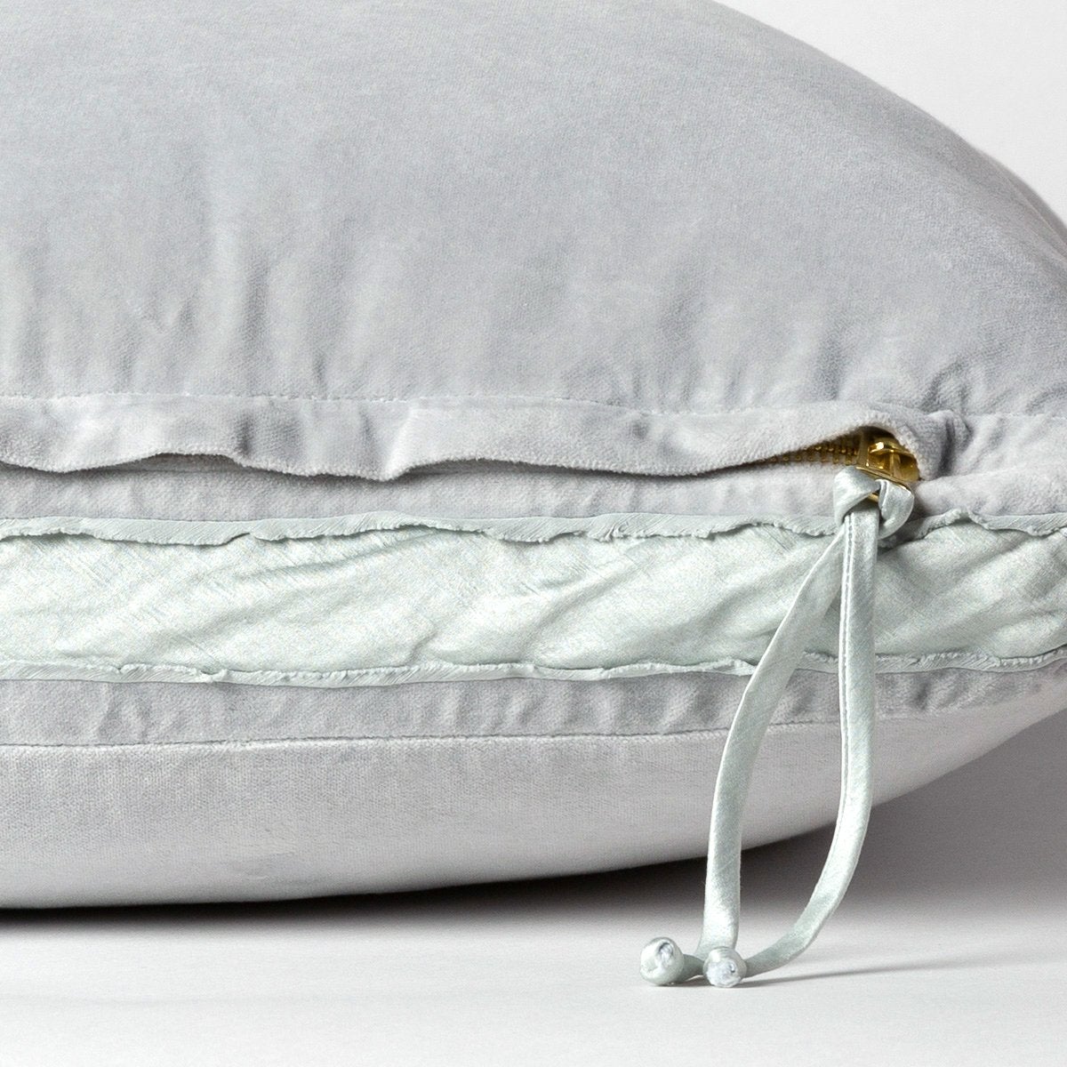 : Close-up of charmeuse gusset, raw-edge trim, and brass zipper detail  on cloud Harlow pillow - cloud, side view.