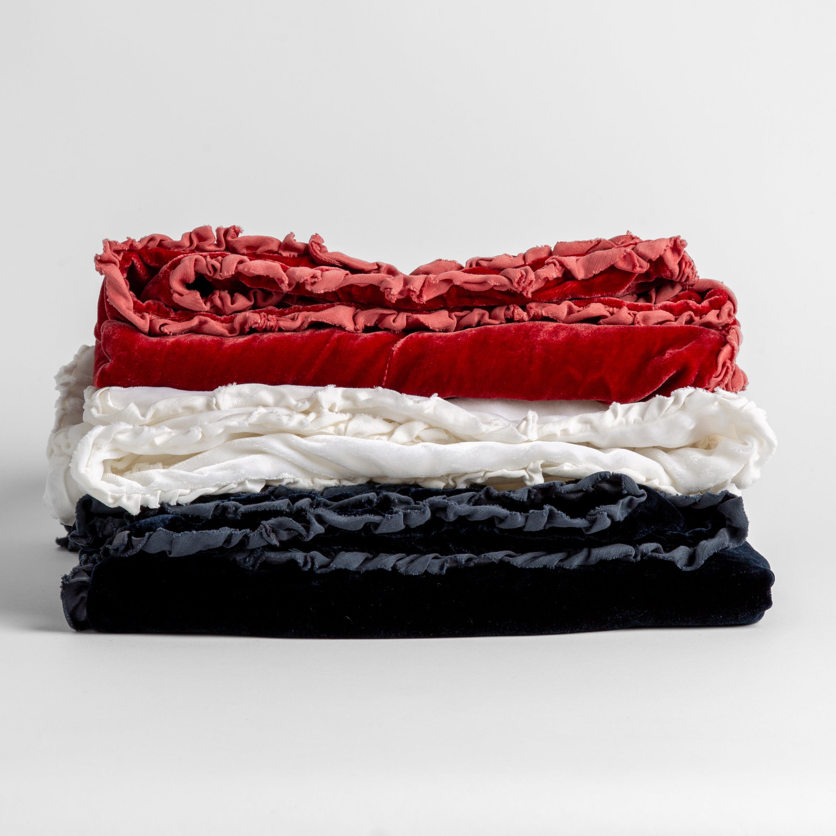 Stack of four silk velvet baby blankets with charmeuse trim shown against a white background.  Blankets shown in Poppy, White and Midnight. 