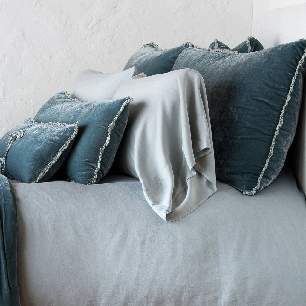Mineral: Silk velvet shams with a petite ruffle on monochromatic bed, leaning upright behind sleeping and throw pillows - side view.