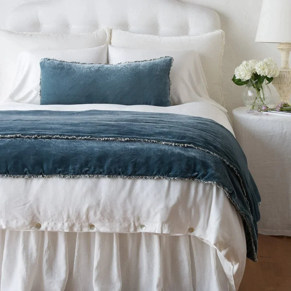 Mineral: Silk velvet shams with a petite ruffle on a white bed, stacked behind sleeping and throw pillows - view from end of bed.