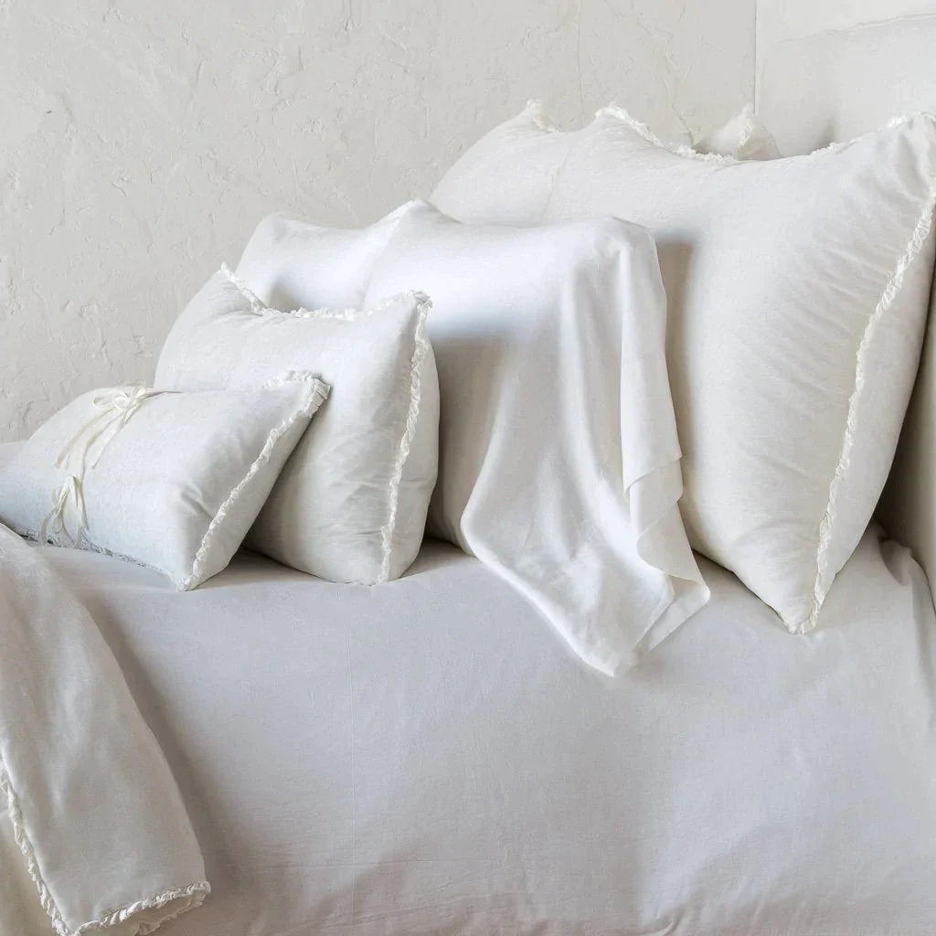Winter White: Silk velvet shams with a petite ruffle on monochromatic bed, leaning upright behind sleeping and throw pillows - side view.