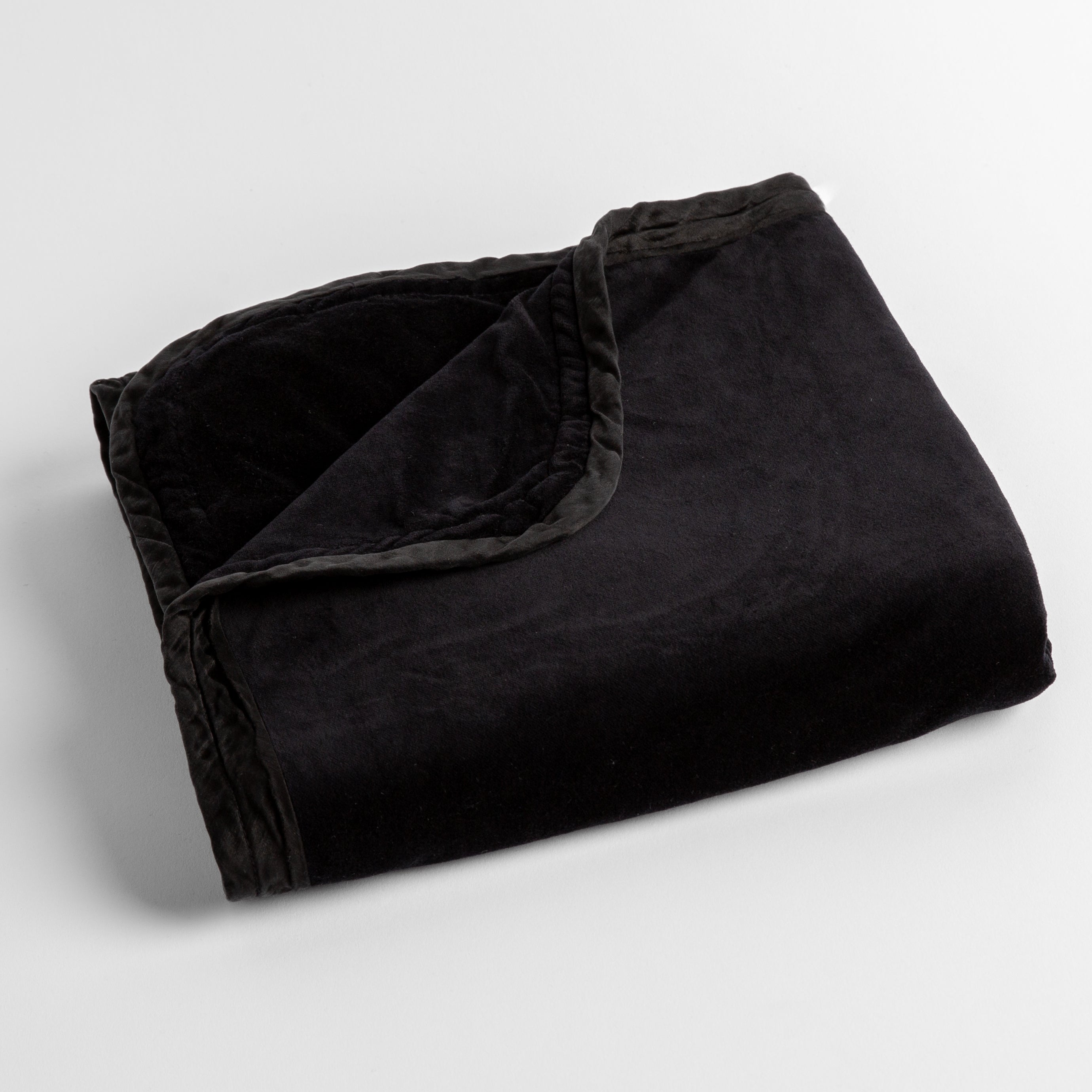 Corvino: cotton velvet baby blanket trimmed with charmeuse, folded with a covern folded back to show trim contrast; shot overhead and at a slight angle against a white background. 